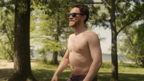 A young man catches and throws a frisbee next to a lake on a summer day 스톡 동영상 116768463