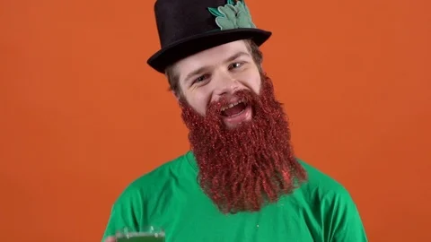 Young man celebrating saint patrick's day isolated on orange holding a glass of Stock Footage 85910746