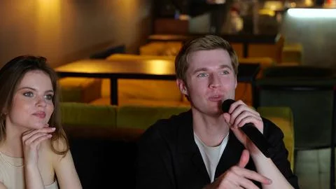 Young man celebrating while singing karaoke song, holding microphone, sitting Stock Photos