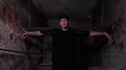 A young man is chained to horizontal handcuffs in a dark quest room. Stock Footage 310656233