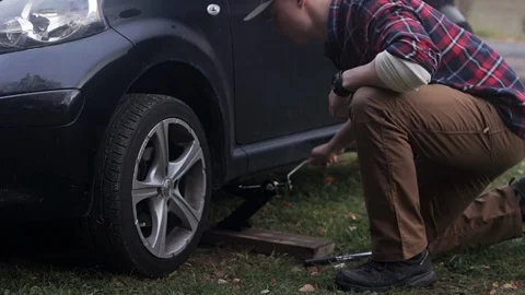 Young man changes tires for the first time, jacking up car and loosening lugnut Stock Footage 97446431