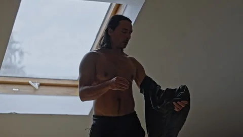 A Young Man is Changing His Clothes in a Brightly Lit Room Filled with Ample 스톡 동영상 303491578