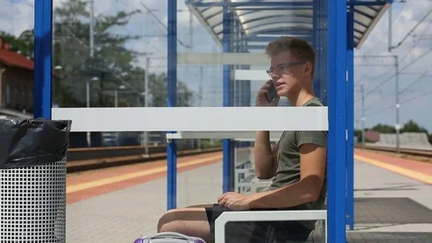 Young man chatting on cellphone while sitting on the train stop Stock Footage 78655089