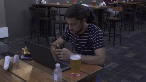 Young man chatting with mobile and computer in bar Vidéo 153107948