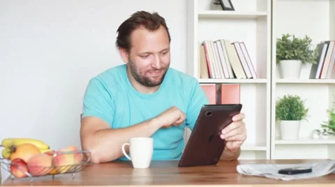 Young man chatting on tablet computer by the table in home Stock Footage 8608190