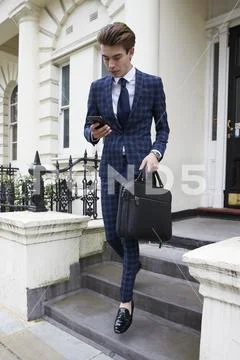 Young man in checked suit looking at phone, leaving building Stock Photos
