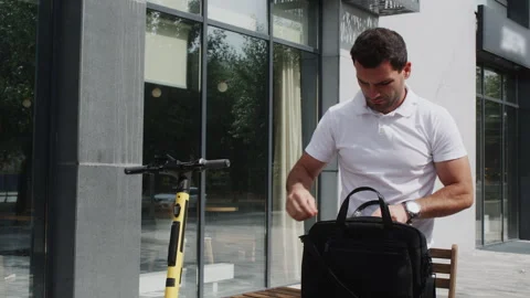 Young man checking bag at outdoor cafe, urban mobility Stock Footage 329187001