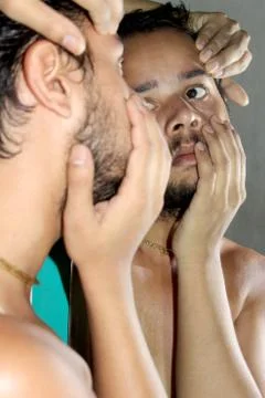 Young man checking his eye on mirror Stock Photos