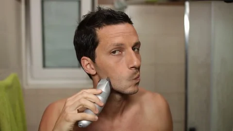 Young man checking his face in the morning, before using the electric shaver. Stock Footage 79490940