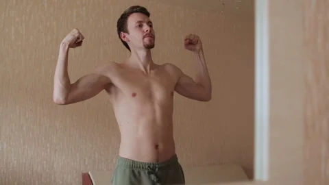 Young man checking his muscles in front of a mirror in the living room. Healthy Stock Footage 265017328