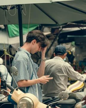 Young man checking phone next to scooter under umbrella in Stock Photos