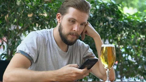 Young man checking smartphone having a beer Stock Footage 125653799