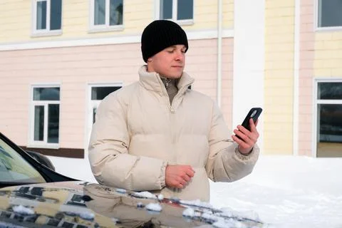 Young man checking smartphone notifications while standing outdoors next to.. Stock Photos