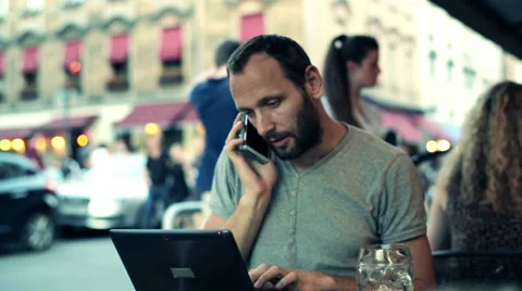 Young man checking something on laptop while talking on the phone in cafe HD Stock Footage 39407378