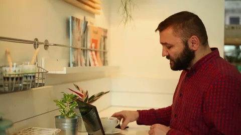 Young man checking something on laptop while talking on the phone in cafe Stock Footage 70859037