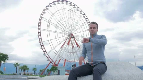A young man checks the messages on the smart watch around the Ferris wheel Stock Footage 67611331