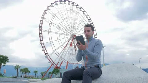 A young man checks the messages on the Tablet PC around the Ferris wheel. Early Stock Footage 67611167