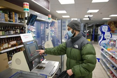 Young man checks out at a self service till in Tesco with face covered Stock Photos