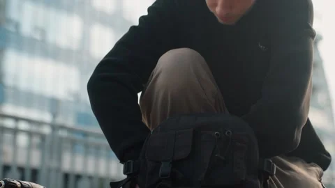 Young man checks small device. Kneeling youth inspects compact electronic gadget Stock Footage 345153541