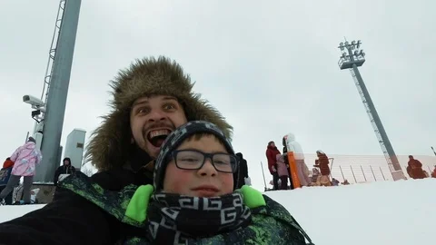 A young man with a cheerful boy with a roller coaster ride in the winter on the 스톡 동영상 100832946
