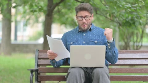 Young Man Cheering while Working with Laptop and Documents Outdoors Video stock 311373760