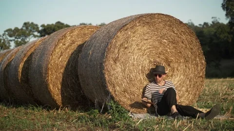 A young man chill in the field. A man in a stripe shirt and a black hat sitting Stock Footage 134517464