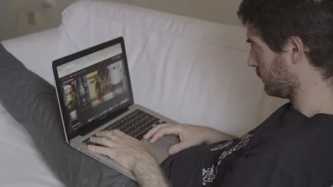 Young Man Chilling In His Sofa Is About to Pick A Movie In His Laptop Stock Footage 137438623