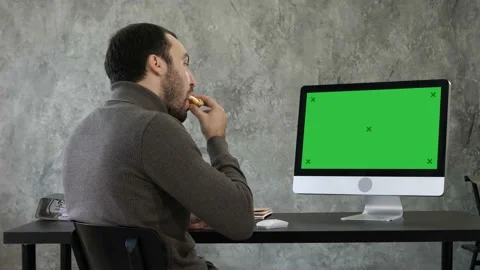 Young man choking while eating and watching something on the computer in the Stock Footage 98984525