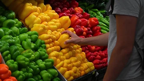 Young man chooses fresh vegetables in a grocery store. Customer takes a bell Stock Footage 244878433