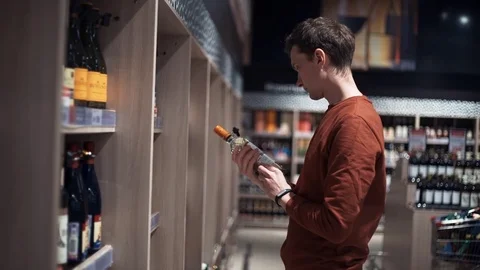 Young man chooses wine looking at bottles at supermarket Stock Footage 82990697