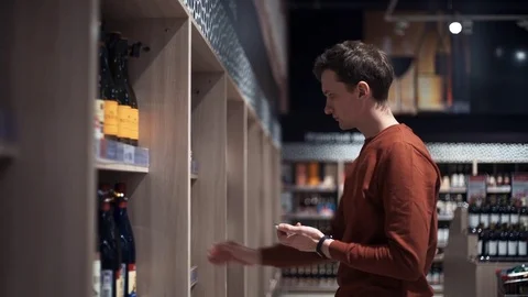 Young man chooses wine taking photo of bottles at supermarket Stock Footage 82990778