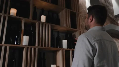 A young man chooses wine while standing near a high shelf with many bottles. Stock Footage 139587043