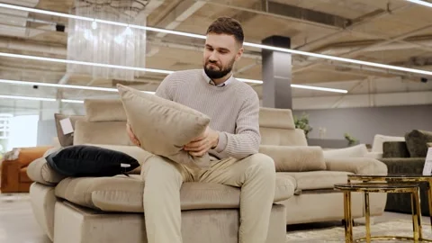 Young man choosing a comfortable beige pillow while shopping for home decor Stock Footage 334654150