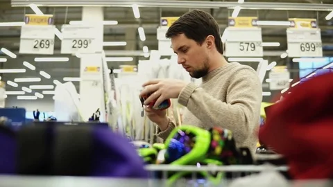 Young man choosing snowboard glasses in the hypermarket. Stock Footage