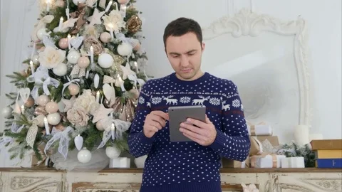 Young man in Christmas knitwear checking up his tablet Stock Footage 70893003