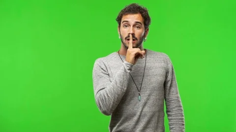 Young man on chroma green screen keeping a secret or asking for silence Stock-Footage 97706518