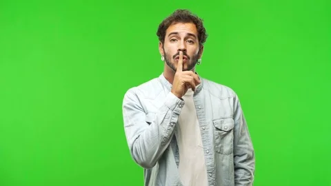 Young man on chroma green screen keeping a secret or asking for silence Stock Footage 97708165