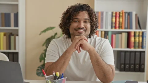 Young man with clasped hands smiling at desk with laptop and pens in a buil.. Stock Footage 337402883