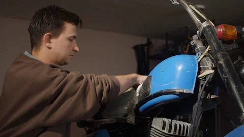 Young man cleaning and maintaining an old blue motorcycle in a garage Stock Footage 342767882