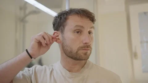 Young man cleaning his ear with a cotton bud in the bathroom, feeling both Stock Footage 335374034