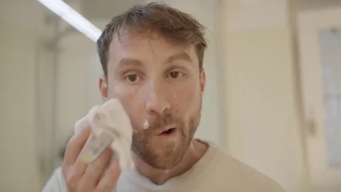Young man cleaning his face with a towel after shaving his beard in the bathroom 스톡 동영상 335204112