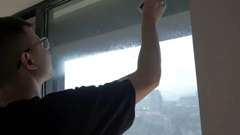 Young man cleaning the wide window glass with magnetic brush. Urban view Video stock 229892878