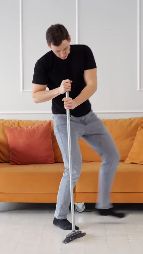 Young Man Cleans Floor With Mop Inside Living Room, Dancing Playfully While Stock Footage 346989223