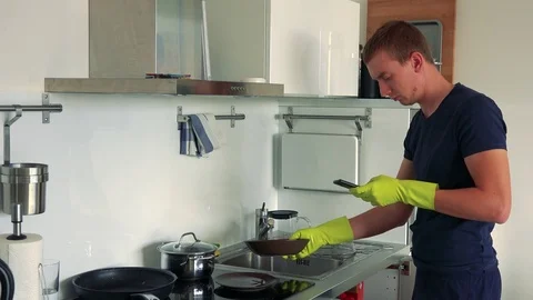 Young man cleans the kitchen (washes dishes) in apartment and works on the 스톡 동영상 80250081