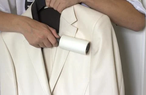 A young man cleans a white jacket with a clothes roller. Stock Photos