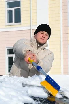 Young man clearing deep snow from a car on a cold winter morning, using a s.. Stock Photos