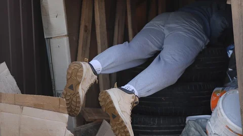 A young man climbed up to get the tools into the garage and stick out his feet Stock Footage 129640585