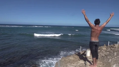 Young Man Climbs Ocean Wall and Raises Hands to the World Stock Footage 79277304