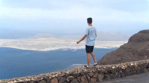 Young man climbs a wall to watch La Graciosa island Stock Footage 136825004