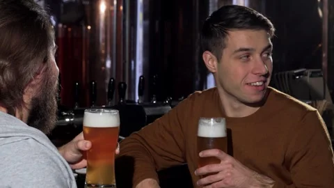 Young man clinking glasses with his friend, savoring craft beer at a cozy pub Video stock 311200411